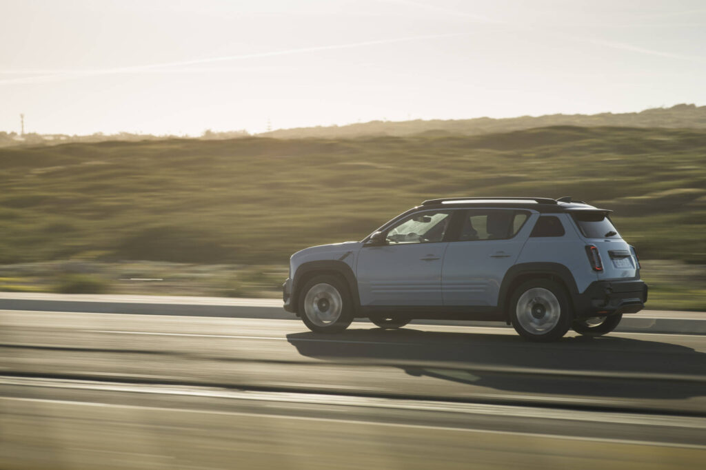 Renault 4 E-Tech Electric in Cloud Blue fährt bei Sonnenuntergang über eine Landstraße – vollelektrisches SUV mit modernem Retro-Design.