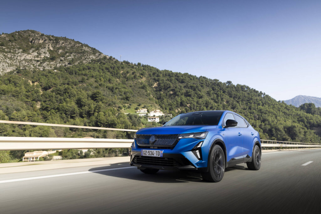 Renault Rafale E-Tech 4x4 300 PS in Atelier Alpine Blau fährt dynamisch auf Bergstraße – sportliches SUV-Coupé mit innovativem Hybridantrieb.